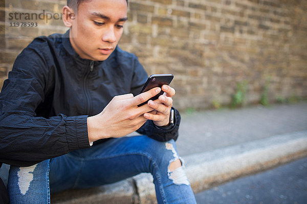 Junger Mann sitzt im Freien und benutzt ein Smartphone