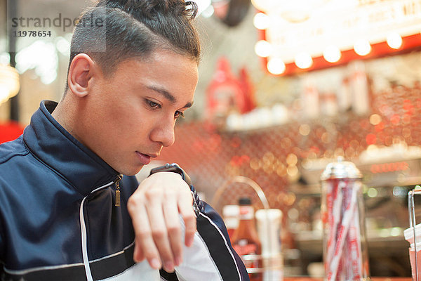 Junger Mann sitzt im Diner und redet in eine Smartwatch