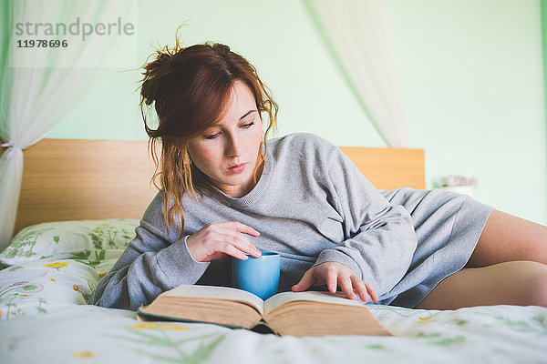 Junge Frau  die auf dem Bett liegt und ein Buch liest