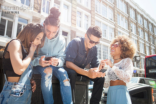 Vier junge Freunde im Freien  die sich ein Smartphone anschauen
