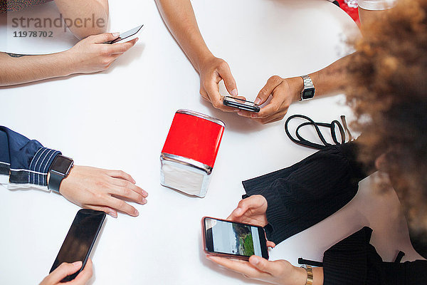 Gruppe junger Freunde am Tisch sitzend  mit Smartphones  Mittelteil