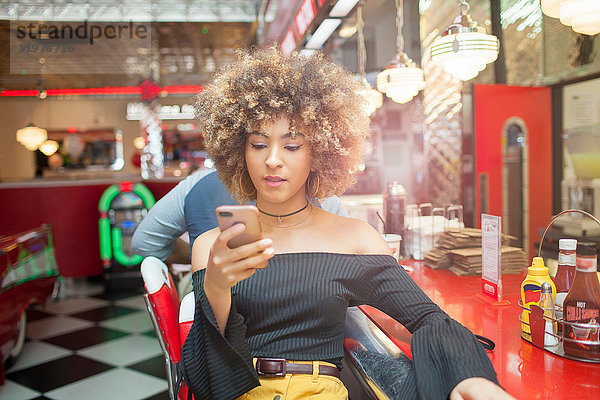 Junge Frau sitzt im Diner und schaut auf ein Smartphone