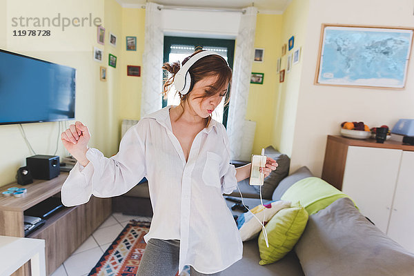 Junge Frau im Wohnzimmer tanzt zu Smartphone-Musik über Kopfhörer