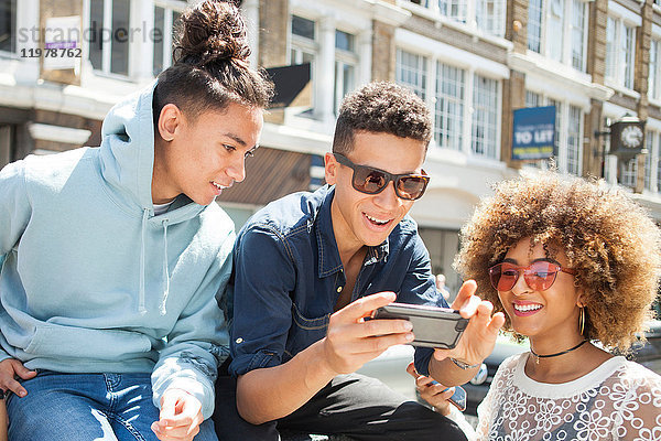 Drei junge Freunde im Freien  die sich ein Smartphone anschauen