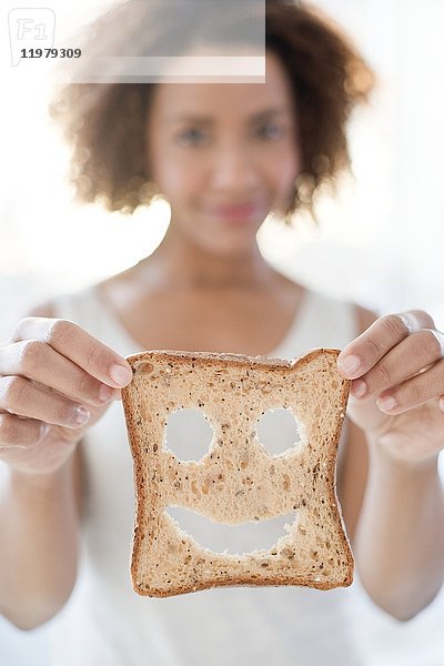 Mittlere erwachsene Frau hält Brot mit Smiley.