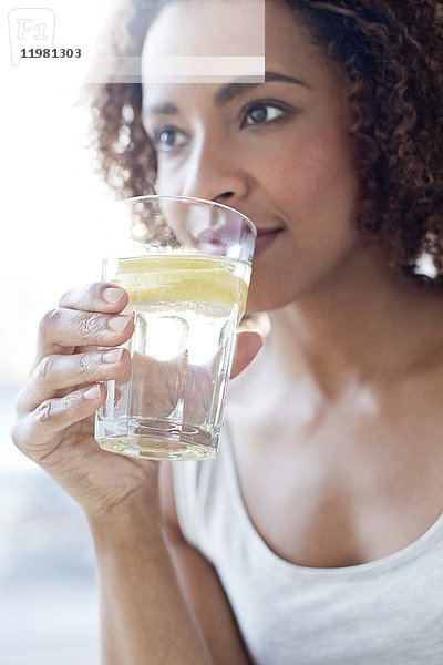Mittlere erwachsene Frau trinkt Wasser mit einer Zitronenscheibe.