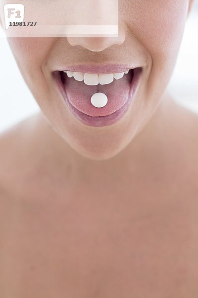 MODELL FREIGEGEBEN. Junge Frau mit Pille auf der Zunge.