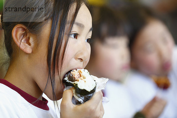Japanisches Grundschulkind beim Essen im Klassenzimmer