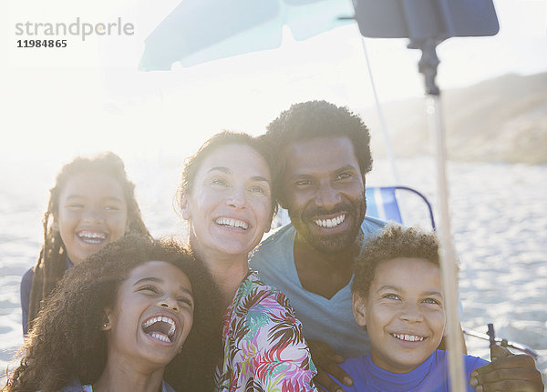 Fröhliche  verspielte multiethnische Familie mit Selfie-Stick am sonnigen Sommerstrand