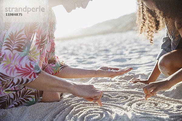 Mutter und Tochter ziehen Spiralen in den Sand am sonnigen Sommerstrand.