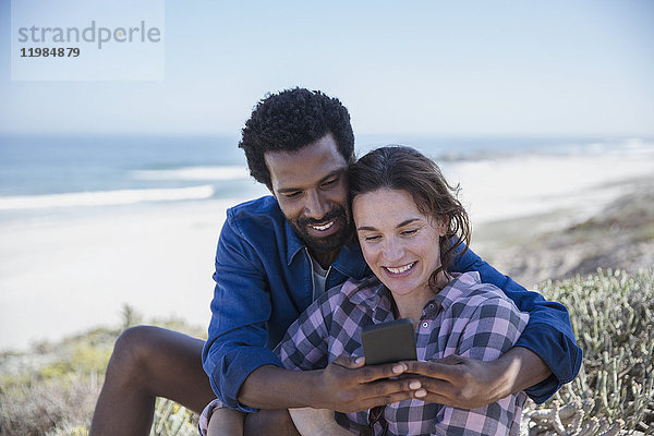 Lächelndes multiethnisches Paar nimmt Selfie mit Handy am Sommerstrand