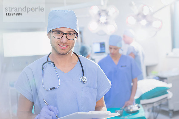 Porträt eines jungen männlichen Chirurgen mit Brille und Klemmbrett im Operationssaal