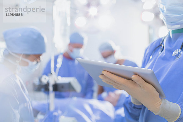 Chirurg mit Gummihandschuhen  der im Operationssaal ein digitales Tablet benutzt