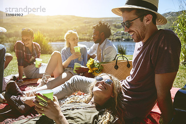 Junge Freunde entspannen sich  genießen ein Picknick am sonnigen Sommerufer des Flusses.