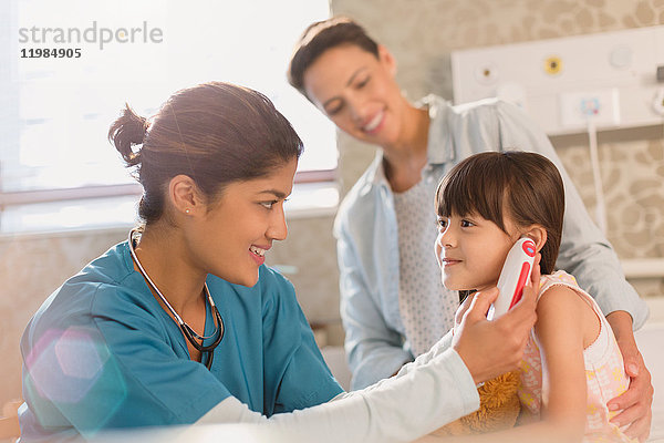 Krankenschwester benutzt digitales Thermometer im Ohr eines Mädchens im Untersuchungsraum