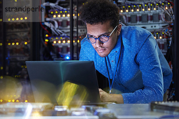 Fokussierter IT-Techniker am Laptop im dunklen Serverraum