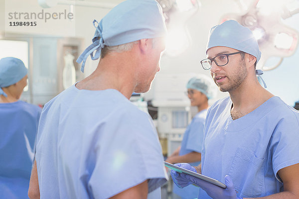 Männliche Chirurgen mit digitalem Tablet im Gespräch im Operationssaal