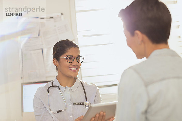 Ärztin mit digitalem Tablet im Gespräch mit einem Patienten im Untersuchungsraum