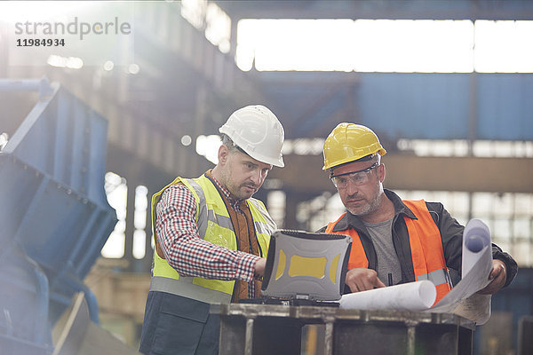 Vorarbeiter und Ingenieur bei der Arbeit am Laptop mit Bauplänen in der Fabrik