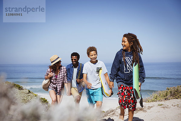 Multi-ethnische Familienwanderung mit Boogie-Boards am sonnigen Sommerstrand des Ozeans