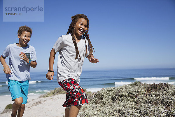 Glückliche Geschwister laufen am sonnigen Sommerstrand des Ozeans