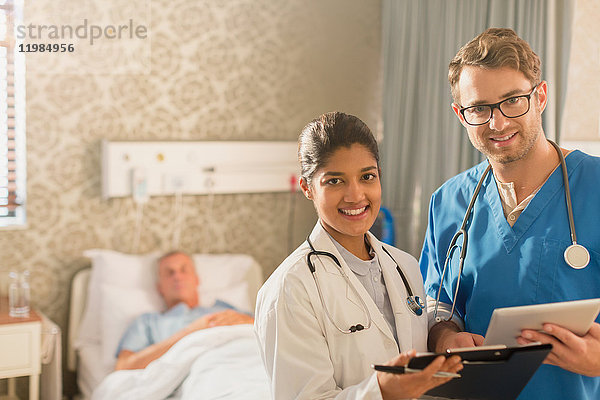 Porträt eines lächelnden  selbstbewussten Arztes und einer Krankenschwester bei der Visite  die ein digitales Tablet und ein Klemmbrett in einem Krankenhauszimmer benutzen