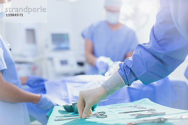 Chirurg mit Gummihandschuhen greift nach einer chirurgischen Schere auf einem Tablett im Operationssaal