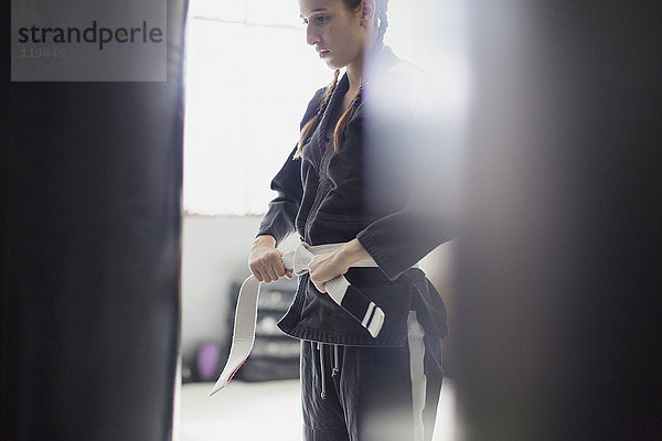 Junge Frau beim Binden des Judogürtels im Fitnessstudio