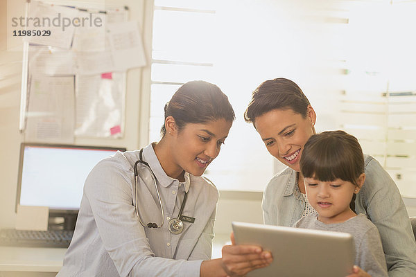 Eine Kinderärztin zeigt einer Patientin und ihrer Mutter im Untersuchungsraum ein digitales Tablet