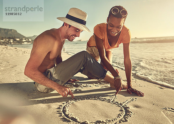 Junges Paar beim Zeichnen im Sand am sonnigen Sommerstrand des Ozeans
