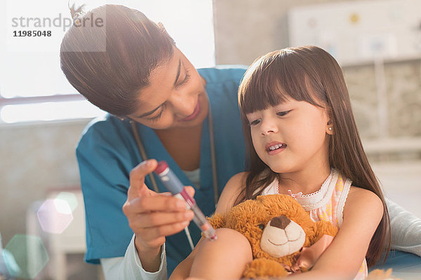 Krankenschwester bringt einem Mädchen mit Teddybär bei  wie man einen Insulin-Pen benutzt