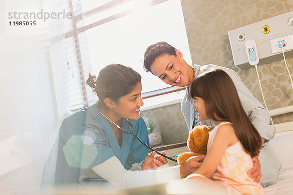 Lächelnde Krankenschwester  die ein Stethoskop bei einer Patientin im Krankenhaus benutzt