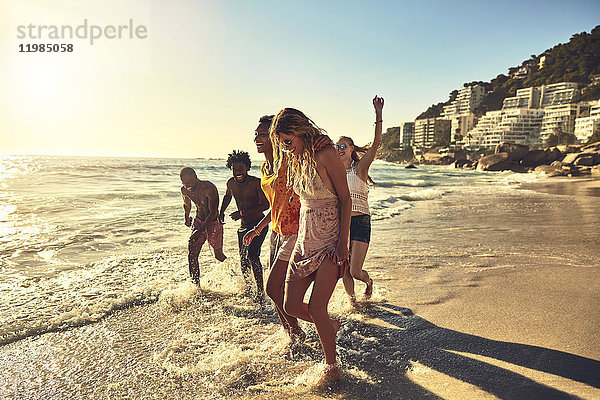 Verspielte junge Freunde beim Spaziergang im sonnigen Sommer auf dem Meer
