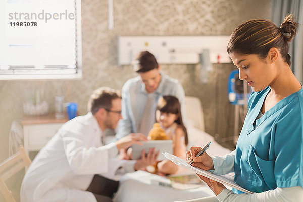 Weibliche Krankenschwester macht sich Notizen auf dem Klemmbrett der Krankenakte  während der Arzt einer Patientin im Krankenhaus ein digitales Tablet zeigt