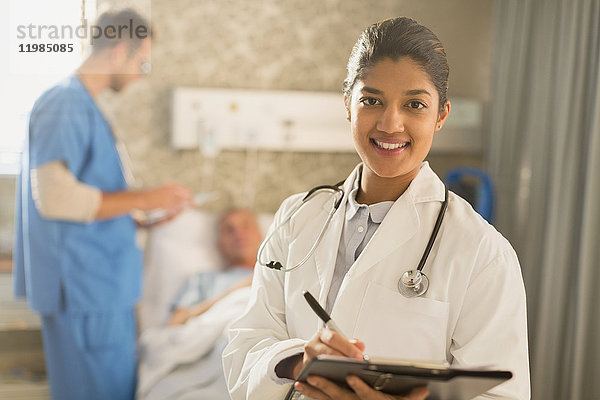 Porträt einer lächelnden Ärztin bei der Visite  die sich Notizen auf einem Klemmbrett in einem Krankenhauszimmer macht