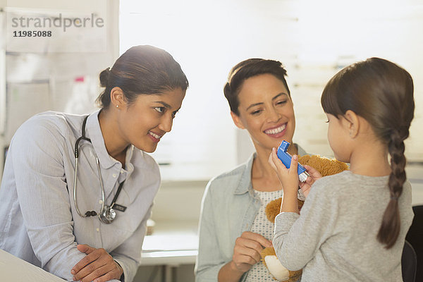 Kinderärztin und Mutter beobachten ein Mädchen  das im Untersuchungsraum einen Inhalator benutzt