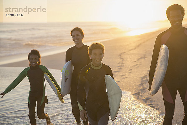 Familien-Surfer beim Wandern mit Surfbrettern am sonnigen Sommer-Sonnenuntergang am Meeresstrand