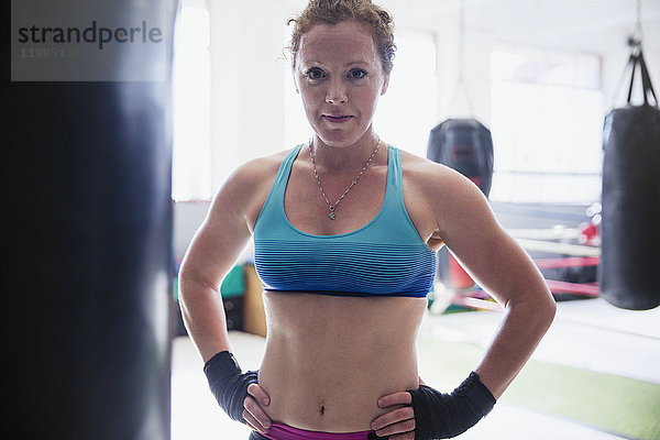 Porträtbewusste  strapazierfähige Boxerin am Boxsack im Fitnessstudio