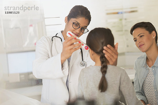 Ärztin mit digitalem Thermometer im Ohr einer Patientin im Untersuchungsraum