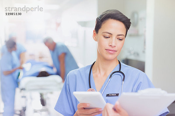 Chirurgin mit digitalem Tablet  die in einem Krankenhauskorridor Papierkram am Klemmbrett überprüft
