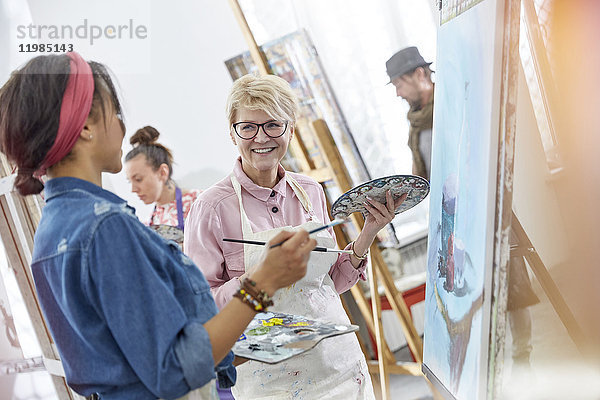 Lächelnde Künstlerinnen mit Pinsel- und Palettenmalerei im Atelier der Kunstklasse