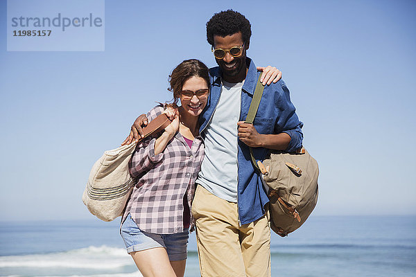 Lächelndes  liebevolles  multiethnisches Paar  das am sonnigen Sommerstrand spazieren geht.