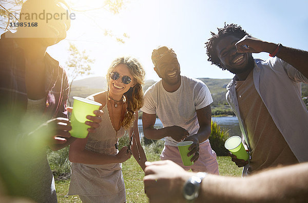 Lachende junge Freunde beim Trinken und Abhängen im sonnigen Sommerpark