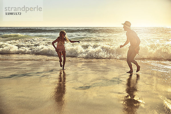 Verspieltes junges Paar  das im nassen Sand am sonnigen Sommerstrand läuft.