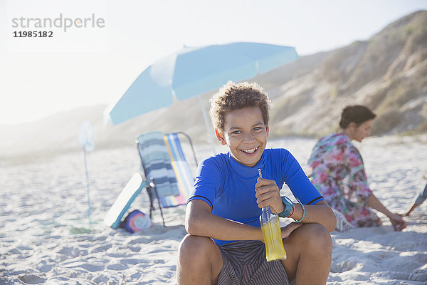 Portrait lächelnd  selbstsicherer Junge trinkt Saft am sonnigen Sommerstrand