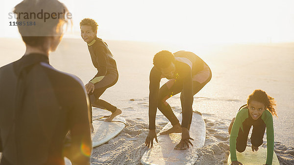 Vater Surfer unterrichtet Kinder beim Surfen auf Surfbrettern am sonnigen Sommerstrand.