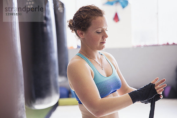 Boxerinnen wickeln Handgelenke neben Boxsack im Fitnessstudio ein