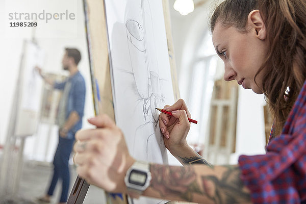Fokussierte Künstlerin mit Tattoo-Skizze an der Staffelei im Kunststudio