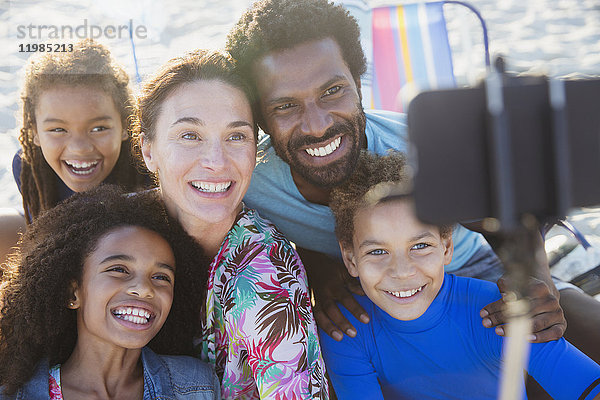 Lächelnde  fröhliche multiethnische Familie  die Selfie mit Selfie-Stick-Kamera-Handy am Strand nimmt.