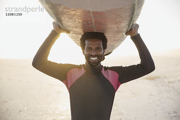 Portrait lächelnder  selbstbewusster Surfer mit Surfbrett am sonnigen Sommerstrand